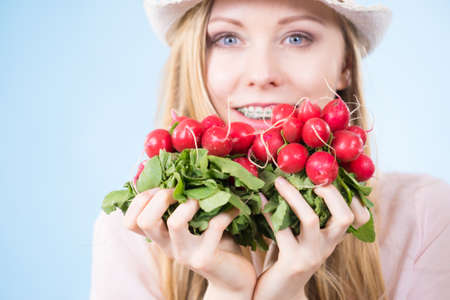 Happy cheerful teenage girl wearing sun hat holding delicious radish close to face. Healthy food.