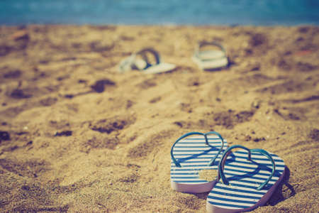 Blue and white flip flops on sand beach during summer time weather.