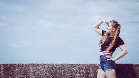 Happy teen woman enjoying her leisure time. Female having long brown hair posing with sky in...
