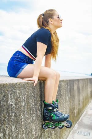 Young woman wearing roller skates outdoor. Fashionable fit girl having fun resting at sunny summer...