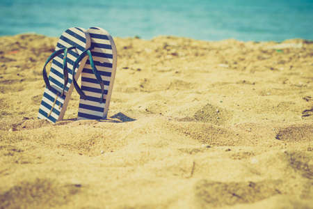Blue and white flip flops on sand beach during summer time weather.の写真素材