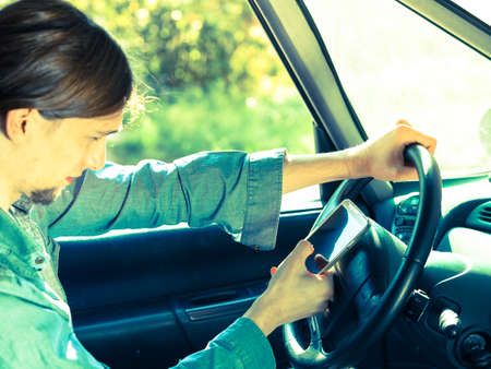Modern technology concept. Man using mobile phone while driving car, checking social media or setting navigation.の写真素材
