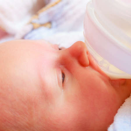 Infant care and feeding concept. Little newborn baby drinking milk from bottle.の写真素材