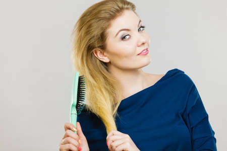 Woman combing her hair with brush. Young female with beautiful natural blond straight long hairs, studio shot on greyの写真素材