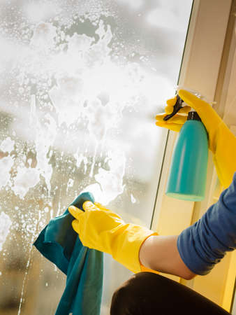 Female hand in yellow gloves cleaning window with blue rag and spray detergent. Spring cleanup, housework conceptの写真素材