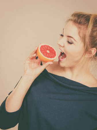 Healthy diet, refreshing food full of vitamins. Happy woman holding sweet delicious citrus fruit, red grapefruit.の写真素材