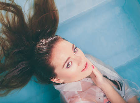 Portrait of sexy seductive woman floating in swimming pool water. Pretty alluring young girl wearing...