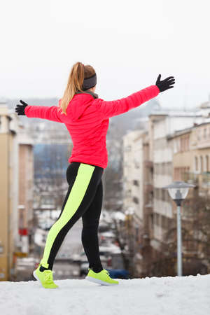 Woman wearing warm sportswear running jogging outside during winter in front of urban city street. Outdoor sport exercises, sporty outfit ideas.の写真素材
