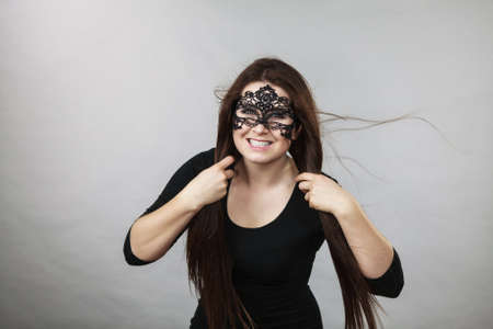 Happy pretty mysterious woman wearing black eye lace mask having tousled windblown long brown hair.