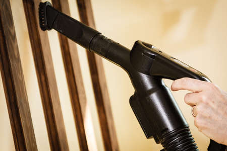 Woman doing house cleaning getting rid of dust on coat hanger using vacuum cleanerの写真素材