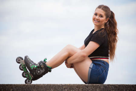 Happy joyful young woman wearing roller skates sitting in town. Female being sporty having fun...