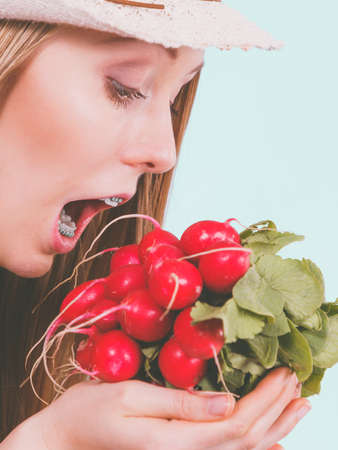 Funny young woman about to bite red delicious radish. Summer vegetables concept.の写真素材