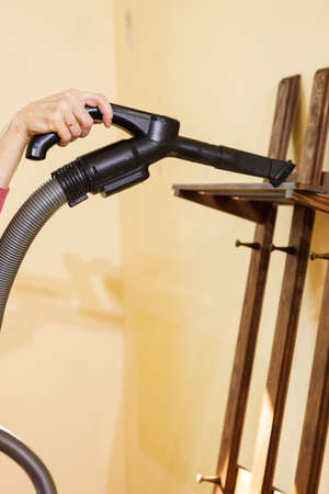 Woman doing house cleaning getting rid of dust on coat hanger using vacuum cleaner