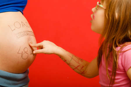 Closeup pregnant woman belly with loading concept painted on her tummy. little girl with amazed face expression pointing on belly her momの写真素材