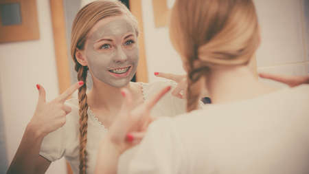 Skincare. Blonde woman in bathroom with grey clay mud mask on her face.の写真素材