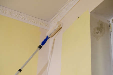Person appplying white paint on yellow wall using roller brush. Home renovation concept.の写真素材