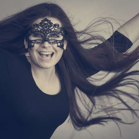 Happy pretty mysterious woman wearing black eye lace mask having tousled windblown long brown hair.の写真素材