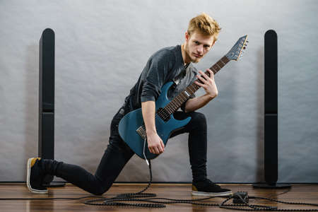 Young bearded man with electric guitar. Adult person in full length is holding instrument and...