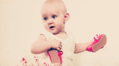 Lesson of walking. Sweet adorable baby girl thinking about make step. Little child toddler wearing princess dress with red small shoes.の写真素材