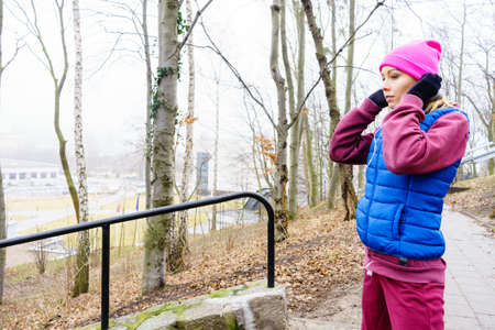 Athlete teen girl wearing warm sporty clothes outside listening to music, city park in the...
