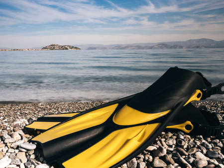 Swimming equipment flippers fins lying on stone beach sea shore. Summer vacation fun concept.の写真素材