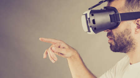 Adult short bearded guy exploring virtual reality wearing VR goggles being into technology pointing...