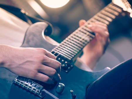Close up of man playing on electric guitar during gig or at music studio. Musical instruments,...