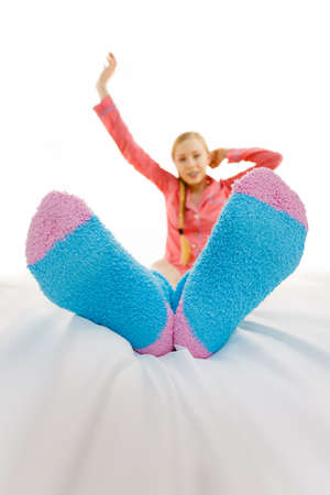 Sleepwear fashion and accessories concept. Woman in pajamas wearing furry warm socks relaxing on bed, feet closeup.の写真素材