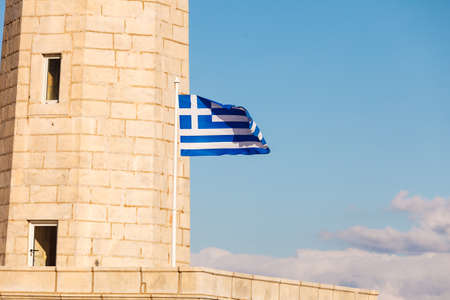 Greek flag and lighthouse near Gythio against blue sky. Laconia Peloponnese Greeceの写真素材