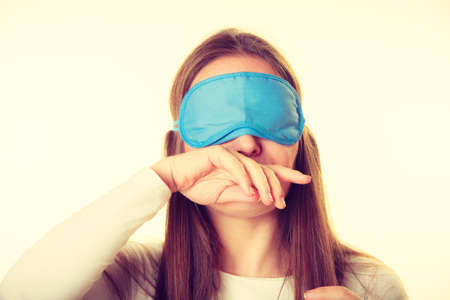 Sleep equipment concept. Portrait of brunette woman sleeping in blue eye mask. Studio shot on beige backgroundの写真素材