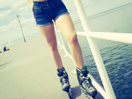 Sexy woman slim legs wearing roller skates standing outside. Sport activity concept.