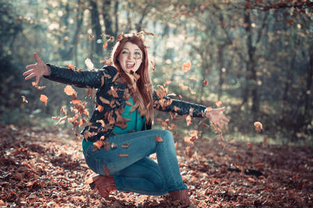 Relax leisure outdoor nature woodland concept. Cheerful ginger woman in park. Young redhead lady having fun with leaves tossing foliage around.の写真素材