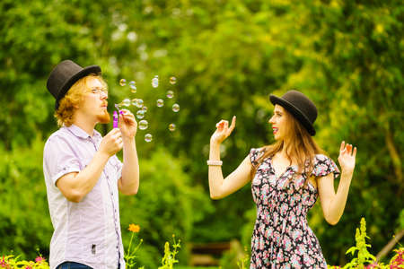 Happy funny hipster couple playing together blowing soap bubbles outdoor in spring park.の写真素材