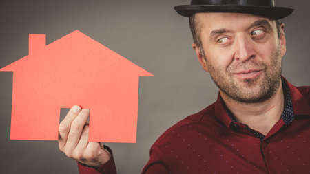 Man wearing fedora hat holding red house model.の写真素材