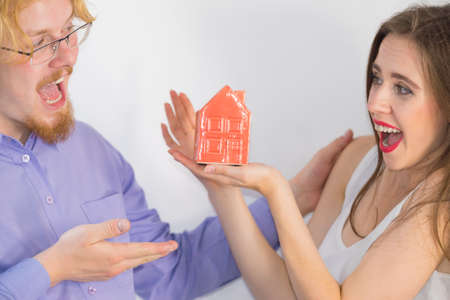 Happy young couple is ready to live together. Man and woman holding small red house model. Home...