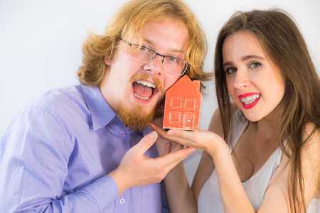 Happy young couple is ready to live together. Man and woman holding small red house model. Home...