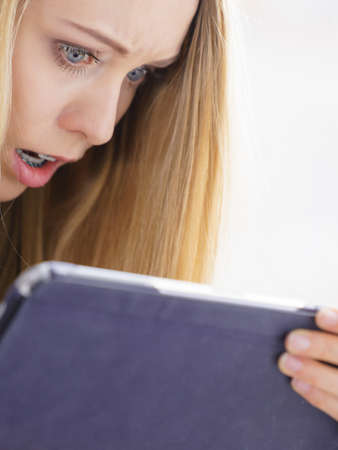 Long hair teen girl watching on tablet pc computer, reading surprising news on internet. Open mouth, shocked astonished face expression.の写真素材