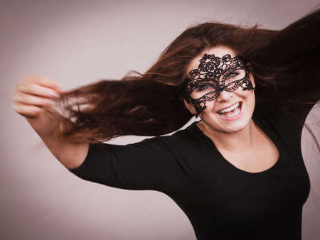 Happy pretty mysterious woman wearing black eye lace mask having tousled windblown long brown hair.の写真素材