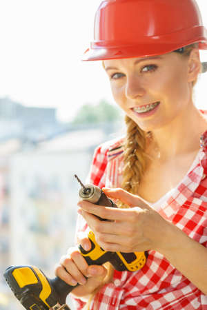 Young woman adjusting, changing her drill bit doing home renovation. Female construction worker having driller tool working on diy.の写真素材