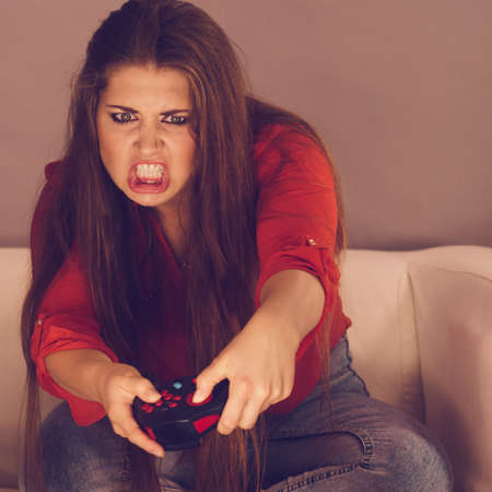 Nerd geek angry adult women playing on the video console holding game pad sitting on sofa. Gaming gamers concept.の写真素材