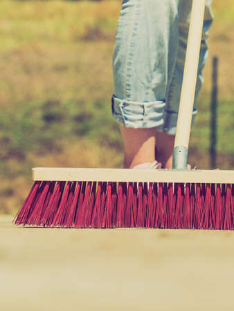Unrecognizable female person using big broom to clean up backyard patioの写真素材