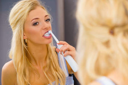 Beautiful blonde woman brushing her teeth using electric toothbrush having fun. Hygiene, body care concept.の写真素材