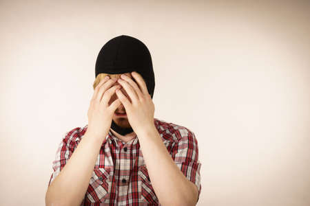 Sad distraught thief wearing black balaclava. Tired man being angry at himslef