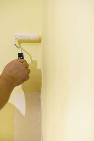 Person appplying white paint on yellow wall using roller brush. Home renovation concept.の写真素材
