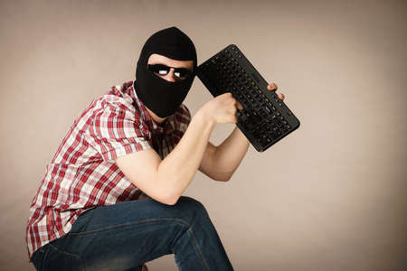 Crazy hacker man. Unrecognizable guy wearing black balaclava holding computer keyboard. Hate speech...