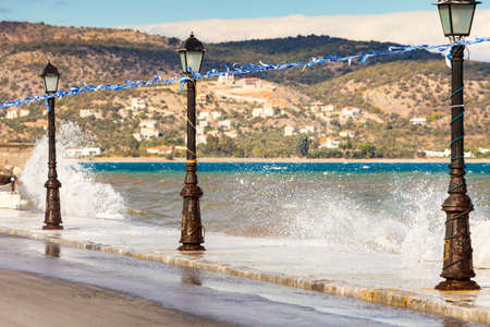Greece, sea coastline in resort village. Promenade walking area on seaside, greek flag and street lamp, waves breaking stone sidewalk, Peloponneseの写真素材