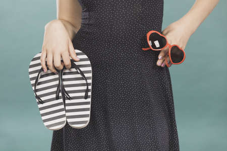 Summer trendy fashionable outfit ideas concept. Woman wearing short navy dress holding flip flops and sunglasses.の写真素材