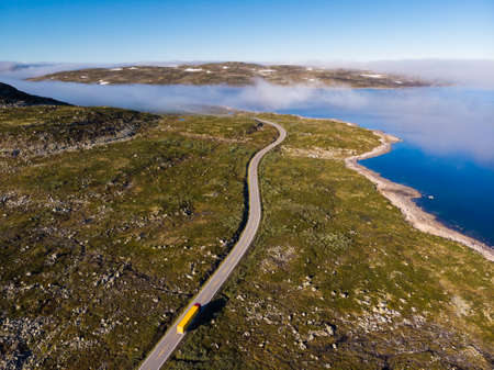 Aerial view. Road crossing Hardangervidda mountain plateau, clouds over lakes, morning time. Norway...