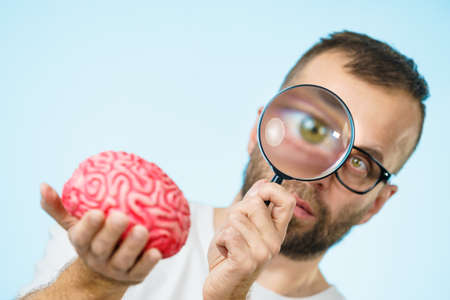 Adult nerd man wearing eyeglasses looking at human brain model. Thinking and intelligence conept