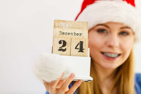 Happy positive young teenage woman wearing Santa hat holding calendar with 24 december date.
